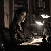 人妻猎人作者暗夜执笔的工作照，在书房灯光下专注写作，气质沉稳而犀利
